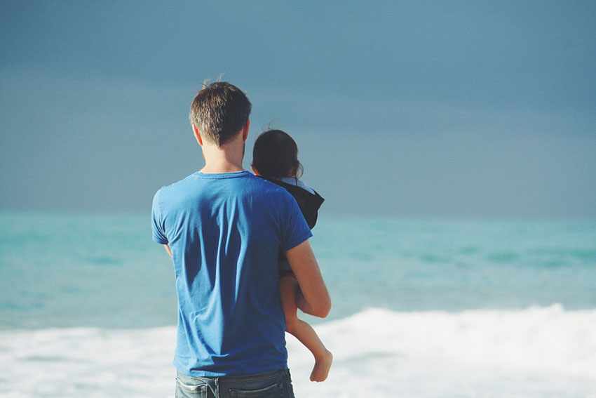 отец держит в руках ребенка на берегу океана