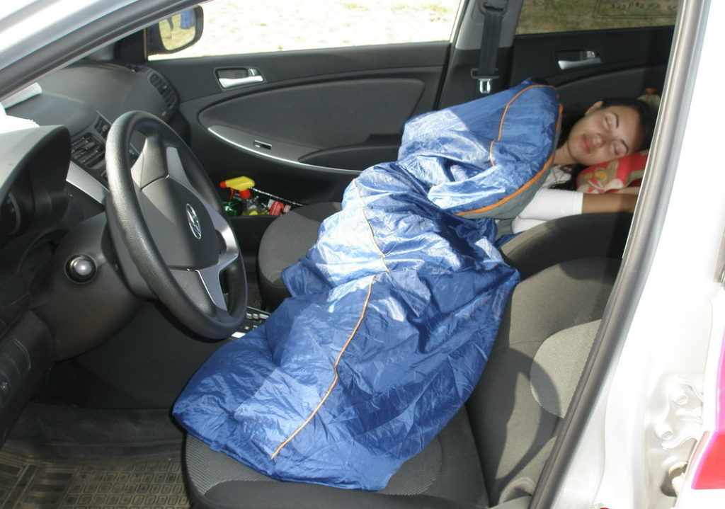 Женщина спит в машине в спальном мешке